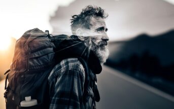An older man with a gray beard and plaid shirt carries a large backpack, walking along a road at sunset. The background blends into a mountain landscape, giving a double exposure effect.