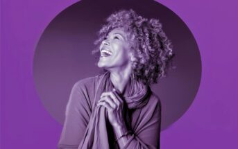 A joyful older woman with curly hair smiles and looks upward, hands clasped in front of her, against a purple background with a darker circle behind her.