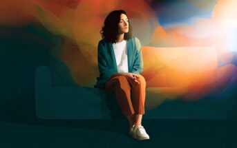 A person with dark hair sits on a couch against a backdrop of swirling, colorful light.
