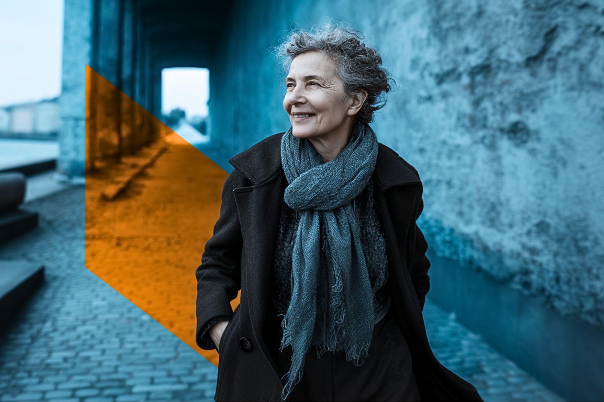 An older woman with curly gray hair, wearing a coat and scarf, smiles while walking on a cobblestone path. A translucent orange geometric shape overlays part of the image, contrasting with the background.