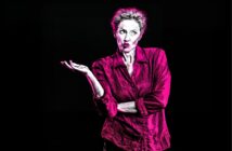A stylized image of a person with short, curly hair wearing a bright pink shirt, raising one hand and shrugging with a puzzled or uncertain expression against a black background.