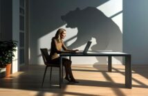 A woman works on a laptop at a desk in a sunlit room, while a large, menacing bear-shaped shadow looms on the wall behind her.