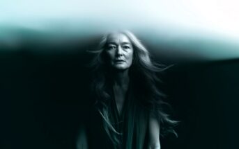 A woman with long flowing hair stands against a dark background, her upper head blending into a misty, ethereal cloud, creating a surreal and dreamlike atmosphere.