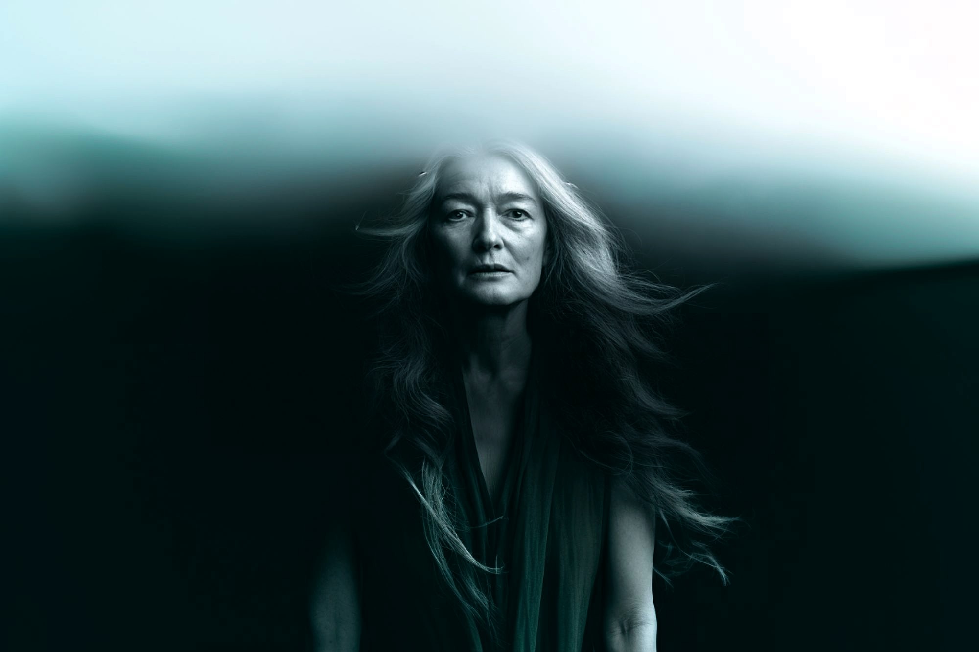 A woman with long flowing hair stands against a dark background, her upper head blending into a misty, ethereal cloud, creating a surreal and dreamlike atmosphere.