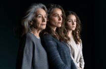 Three women of different ages—an elderly woman, a middle-aged woman, and a young woman—stand in a row against a dark background, gazing thoughtfully into the distance.