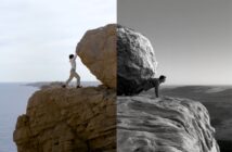 A person pushes a large boulder up a cliff, with the left half of the image in color and the right half in black and white, highlighting the dramatic landscape and effort.