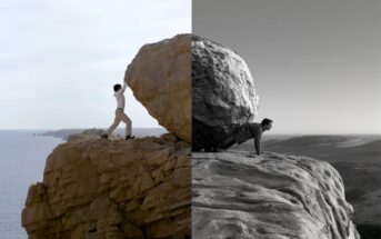 A person pushes a large boulder up a cliff, with the left half of the image in color and the right half in black and white, highlighting the dramatic landscape and effort.