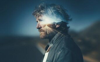 A man with tousled hair and a beard stands in profile, overlaid with a double exposure of a sunlit road leading toward distant mountains, blending his silhouette with the landscape.