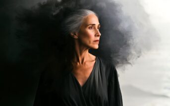 An older woman with long gray hair stands in profile, wearing a dark dress. Dark, smoky clouds swirl dramatically behind her, creating a contrast with the lighter background.