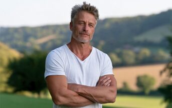 A middle-aged man with graying hair and stubble standing with his arms crossed outdoors.