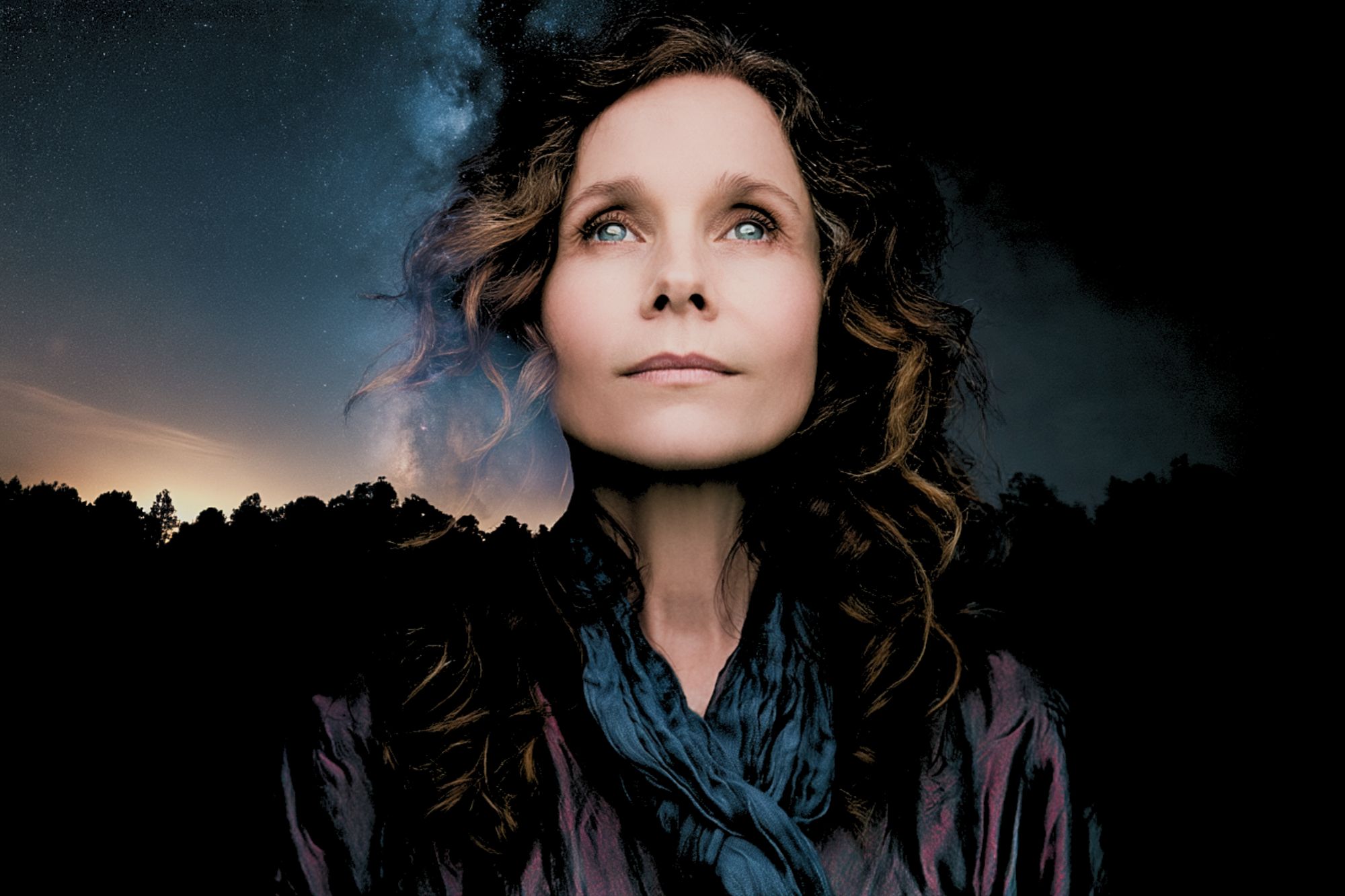 Portrait of a woman looking upward against a background of a starry night sky and silhouettes of trees.