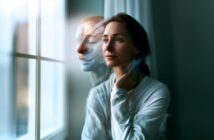 A woman in a white shirt sits by a window, looking outside thoughtfully. A blurred, ghostly double of her face appears beside her, suggesting deep contemplation or emotional distress.