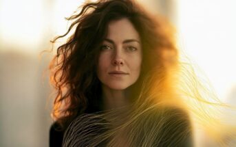 Close-up portrait of a woman with long, dark, wavy hair backlit by golden sunlight.