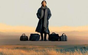 A woman in a long coat and scarf stands outdoors on dry grass with five black travel bags lined up in front of her, against a backdrop of soft hills and a pale sky.