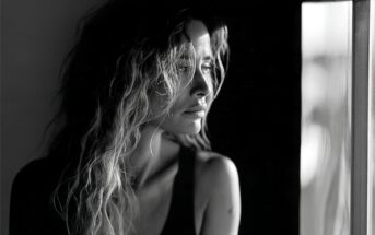 A woman with wavy hair gazes out of a window.