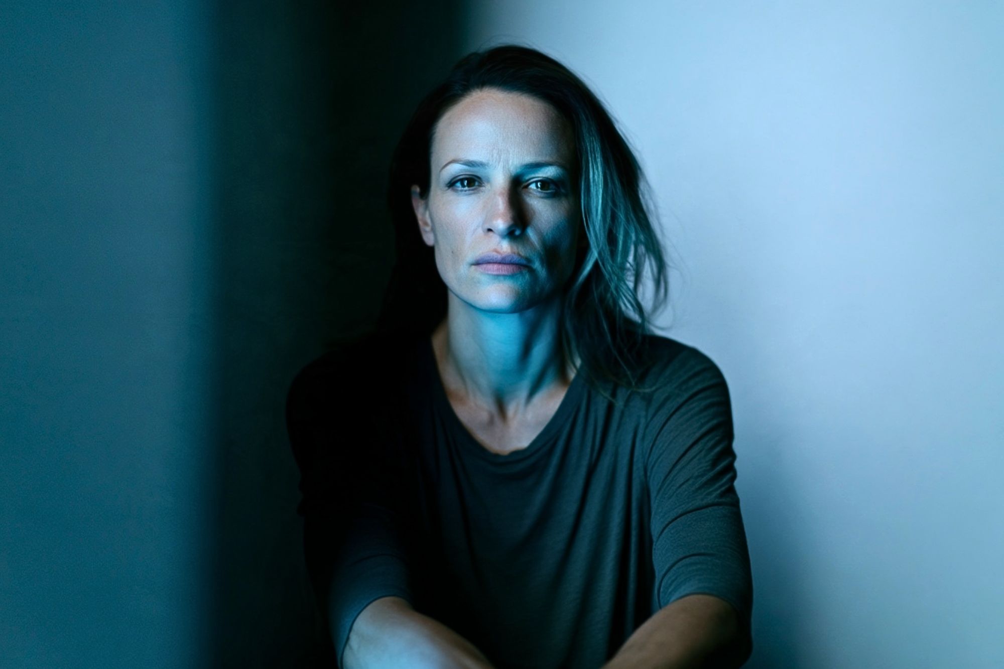 A woman with a serious expression looking directly at the camera in blue-toned lighting.