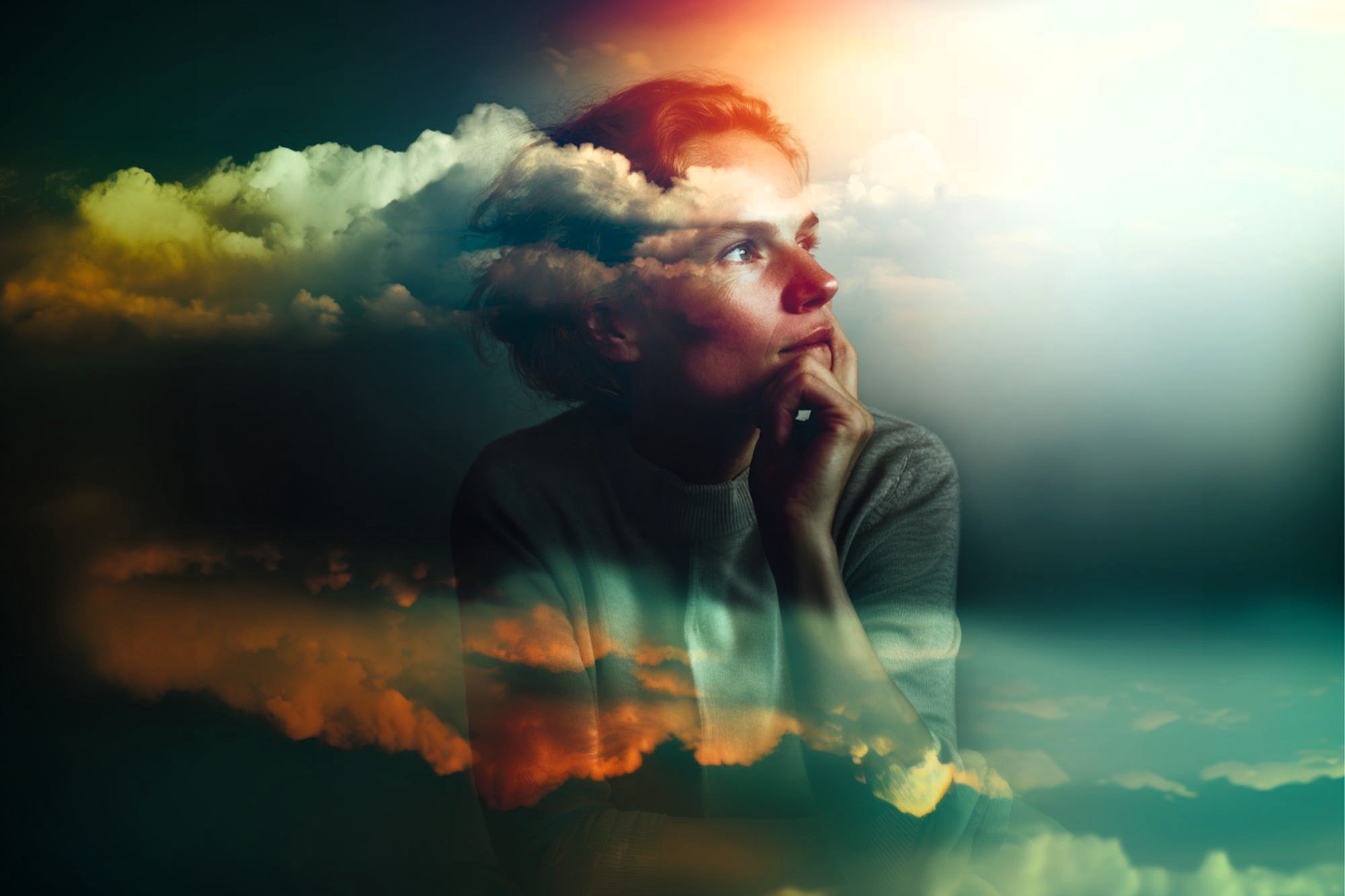 A woman gazes thoughtfully into the distance with her chin resting on her hand. Wispy, colorful clouds are superimposed over her, creating a dreamy, surreal atmosphere with soft light and vibrant hues.