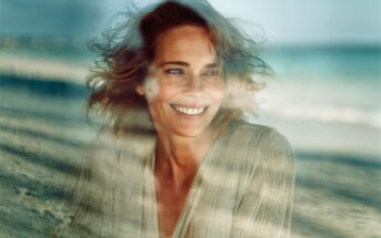 A smiling woman with light brown hair viewed through a soft, double-exposed effect overlaying a beach scene.