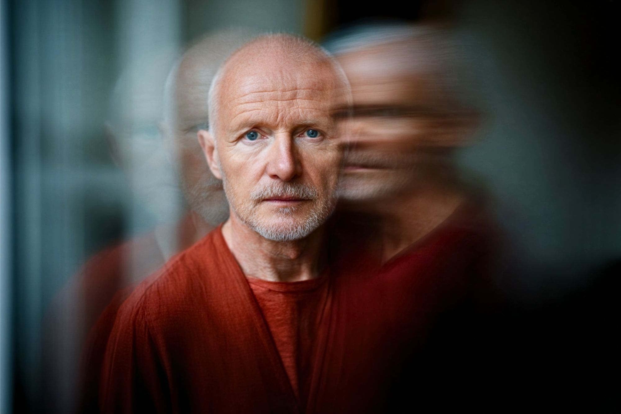 A man with short hair and a light beard wearing a rust-colored shirt, shown with a motion-blur effect.