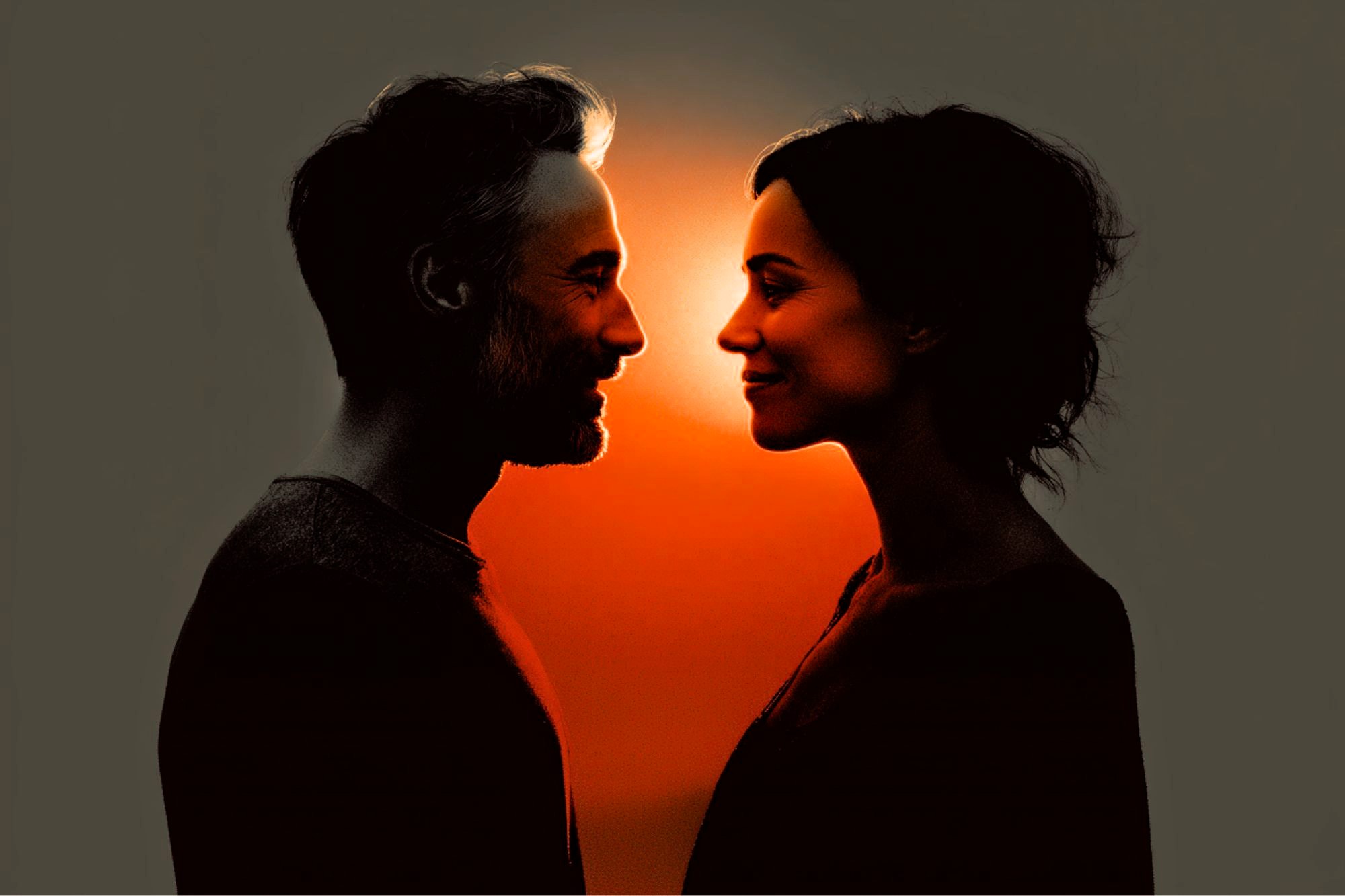 A man and a woman face each other, smiling, with warm orange light glowing between them, creating strong silhouettes against a dark background.