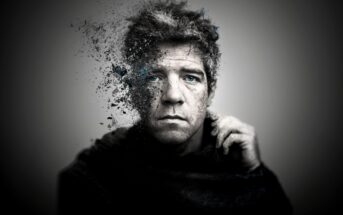 A grayscale portrait of a man with blue eyes, whose left side is dissolving into particles, creating a surreal, fragmented effect against a blurred gray background.