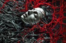 A person with pale skin appears entangled in dark, root-like tendrils and surrounded by vibrant, twisting red veins, creating a surreal and haunting visual effect.