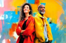 A woman and a man stand back to back, both smiling and wearing bright jackets, with a colorful abstract background in blue, yellow, and orange hues.
