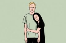 A woman with long dark hair hugs a man with short blond hair. The man stands with a neutral expression while the woman smiles with her eyes closed, leaning her head on his shoulder. The background is pale green.