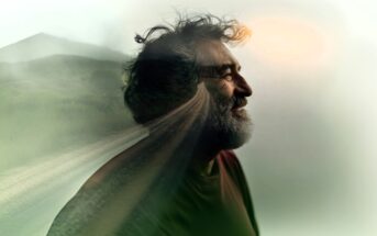 A bearded man smiling in profile, blended with an image of a rural road and landscape, creating a double exposure effect with soft, dreamy lighting.