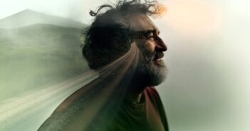 A bearded man smiling in profile, blended with an image of a rural road and landscape, creating a double exposure effect with soft, dreamy lighting.