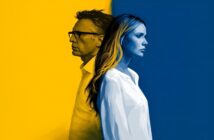 A man and woman stand back to back, divided by a yellow and blue background. The man is on the yellow side facing left, while the woman is on the blue side facing right. Both appear serious and contemplative.