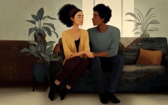 A couple sits together on a sofa, holding hands and looking at each other.